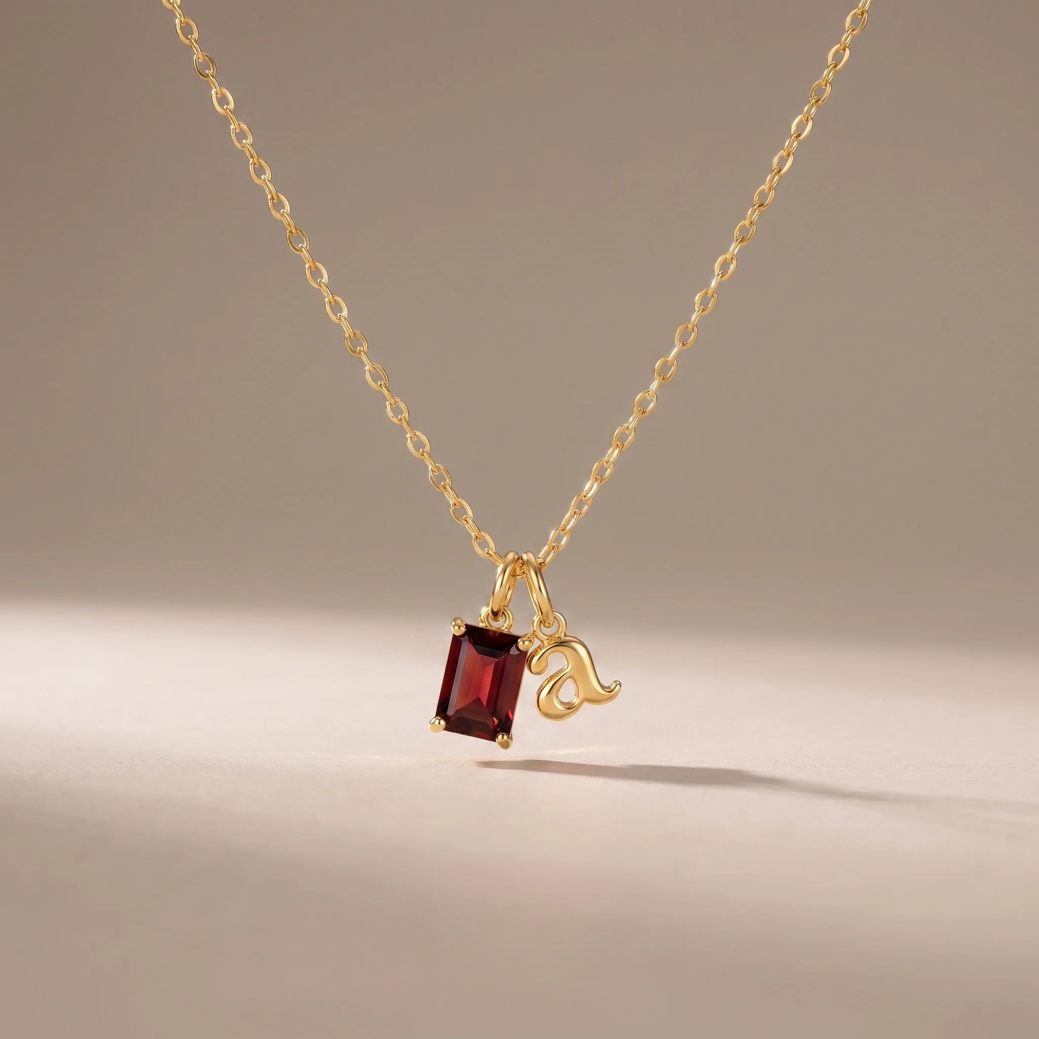 Initial & Birthstone Necklace, a sealed 18K gold personalized initial and birthstone necklace, on a plain background