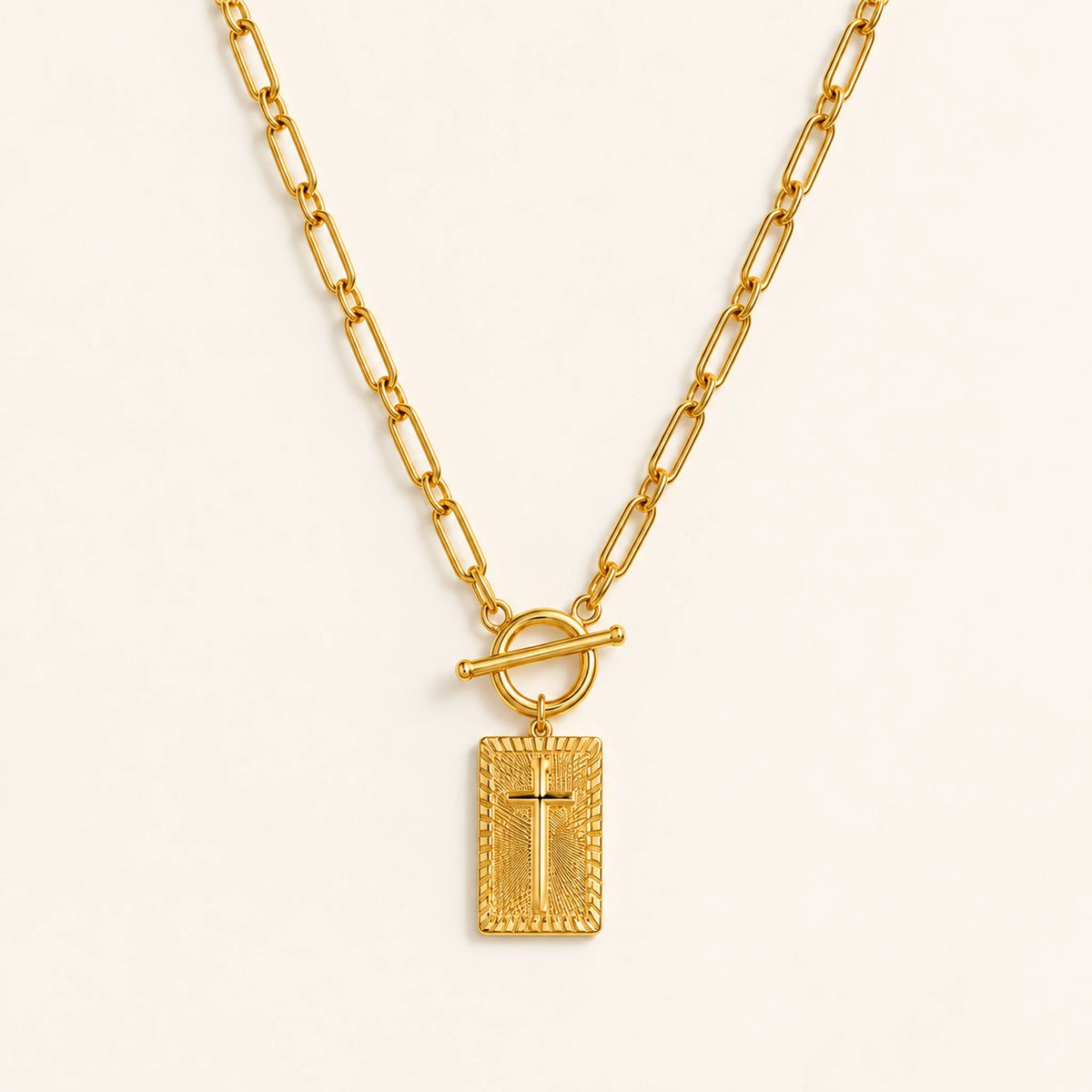 Amada Nail Cross Necklace in gold with a rectangular cross pendant and toggle clasp on an ivory background.