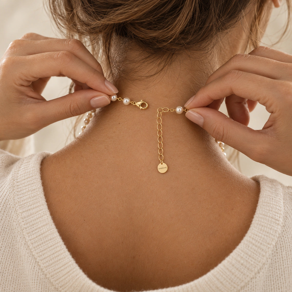 Hands fastening the Pearl Cross of Grace Necklace at the back of the neck.