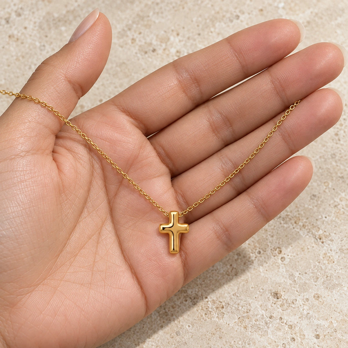 The Bold Cross Necklace held in hand, showing its true scale