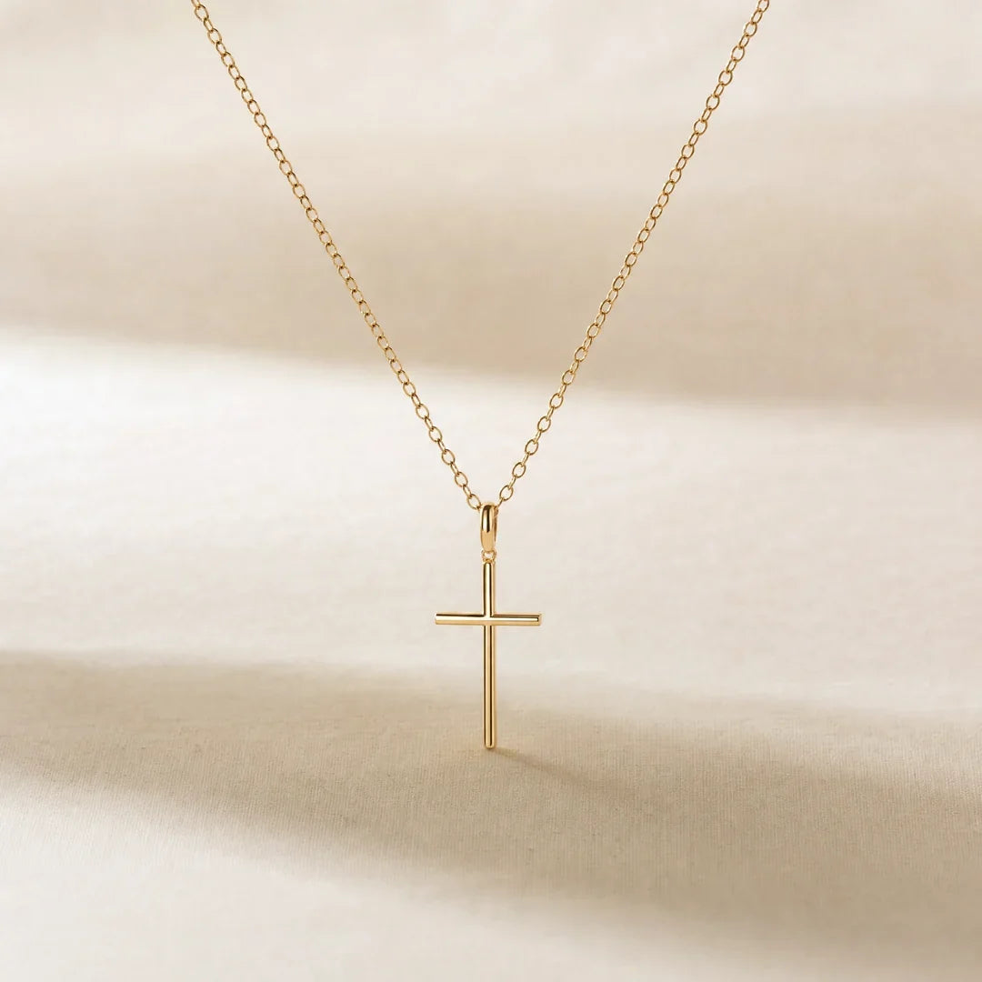 Her First Prayer, a sealed 18K gold cross necklace, on a plain background