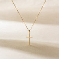 Her First Prayer, a sealed 18K gold cross necklace, on a plain background