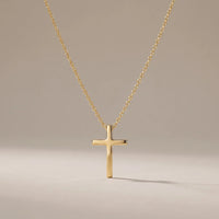 Milestone Cross, a sealed 18K gold cross necklace, on a plain background