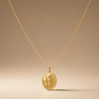 Safe Travels, a sealed 18K gold St. Christopher medal necklace, on a plain background