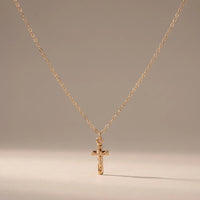 The Vow, a sealed 18K gold crucifix necklace, on a plain background